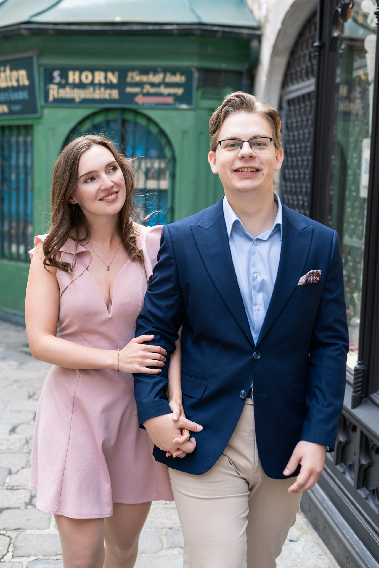 Paarshooting in der Wiener Innenstadt, Mann schaut in die Kamera, Frau schaut Mann verliebt an. Sie halten Händchen.