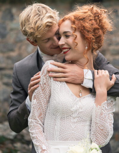 Hochzeitsfoto, Braut steht vor Bräuigam, er hält sie im Arm, sie schauen sich verliebt an